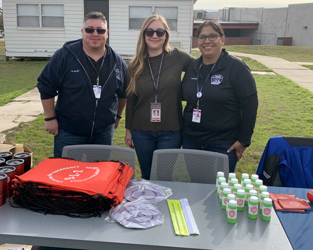 CAPCOG 9-1-1 Senior Training Specialist, Veronica Neal, stands between two Austin Police Department 9-1-1 operators during the APD Cadet's Kids Day. She helped educate children about how to call 9-1-1.